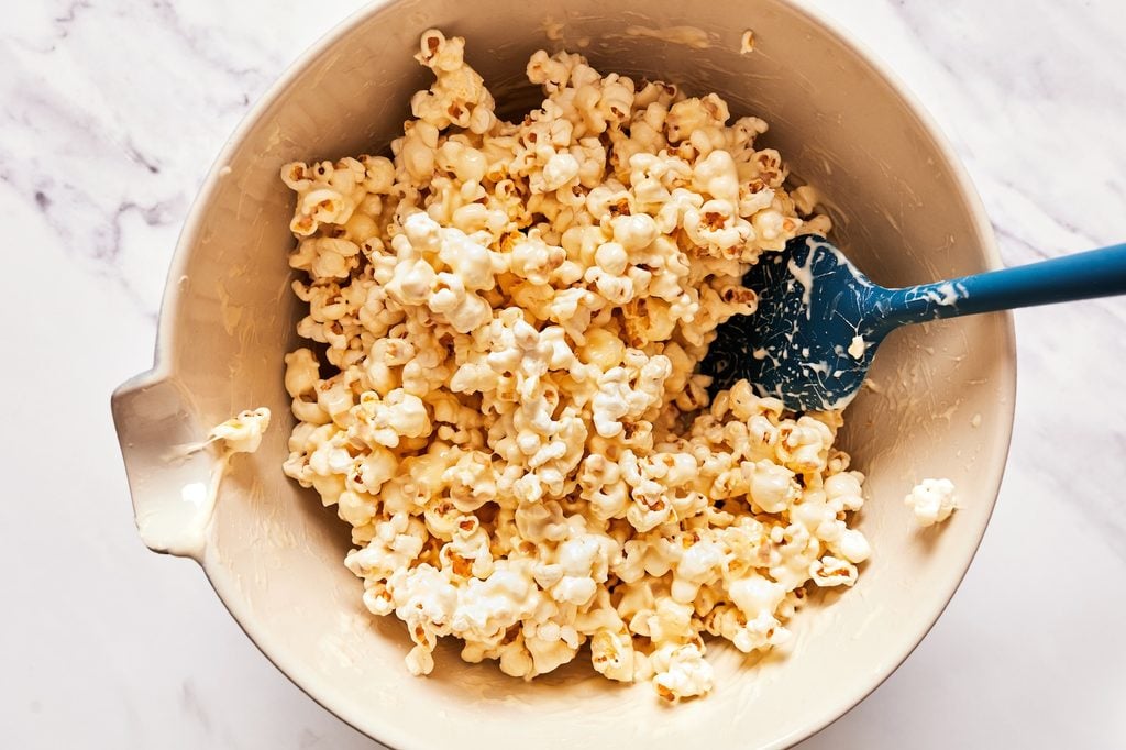 Rubber spatula folding melted marshmallow into popcorn in a large bowl