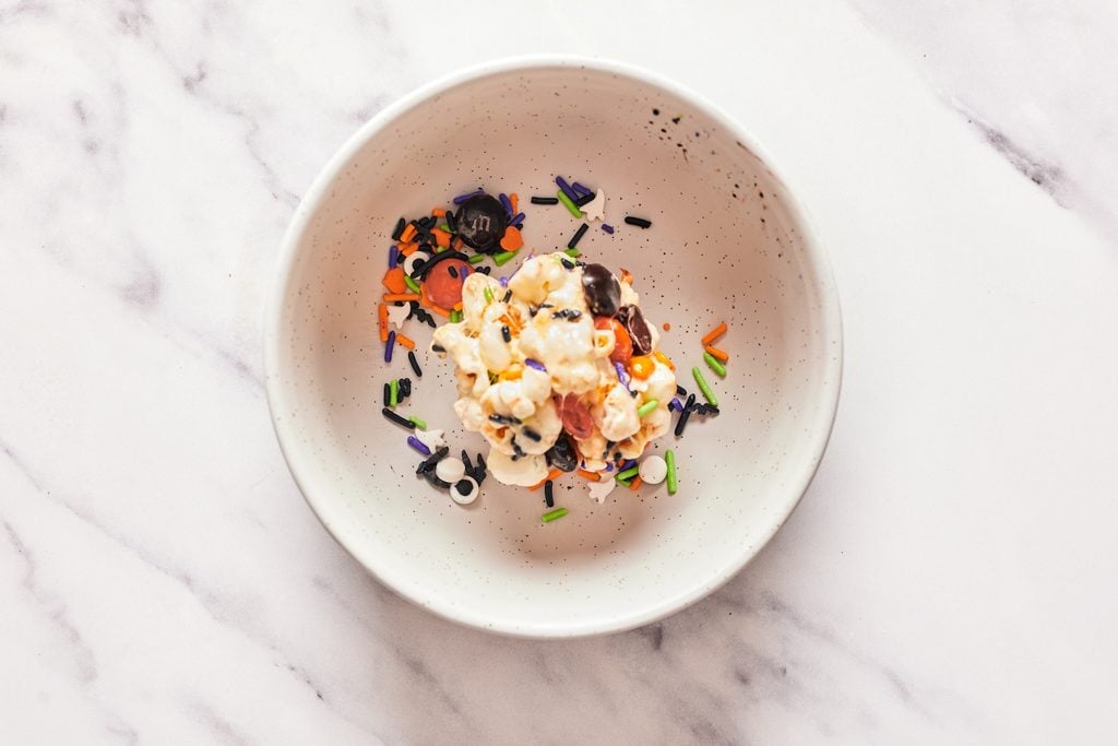 Packing a scoop of marshmallow popcorn into a ball in white bowl