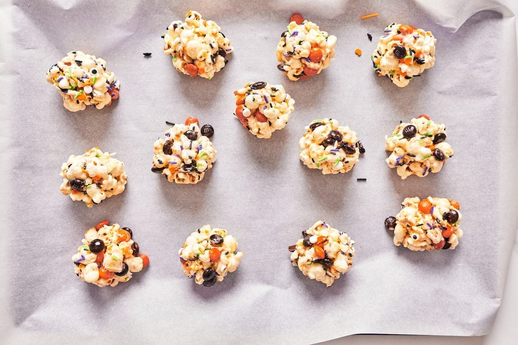 Popcorn ball rolled in Halloween sprinkles resting on a parchment lined baking sheet.
