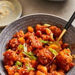 Dakgangjeong tossed in a sweet and spicy sauce in a bowl topped with sesame seeds and green onions.