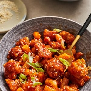 Dakgangjeong tossed in a sweet and spicy sauce in a bowl topped with sesame seeds and green onions.