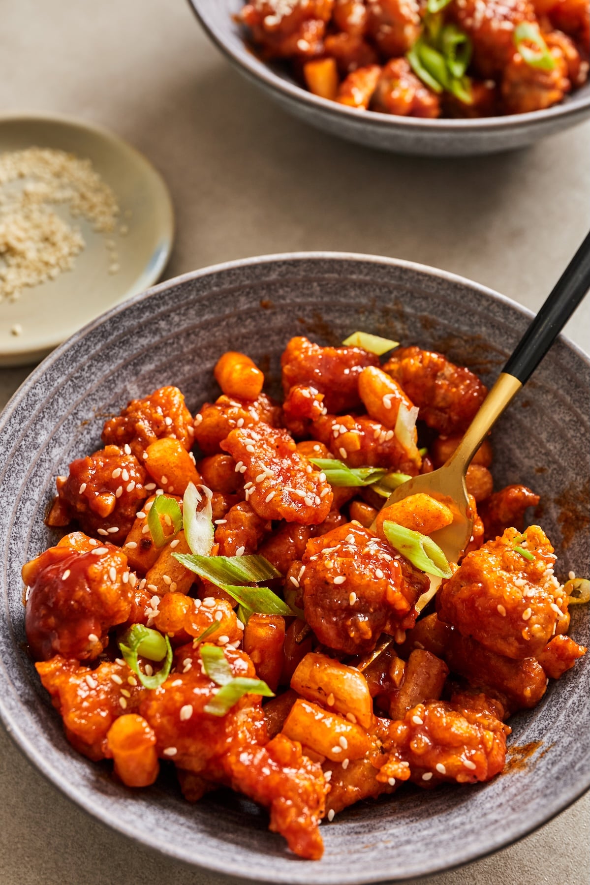 Dakgangjeong tossed in a sweet and spicy sauce in a bowl topped with sesame seeds and green onions.