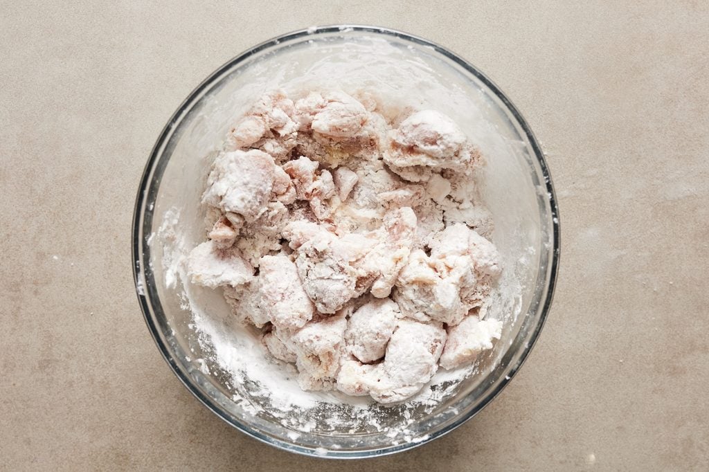 Raw chicken pieces coated in potato starch in a glass bowl before transferring into the air fryer.