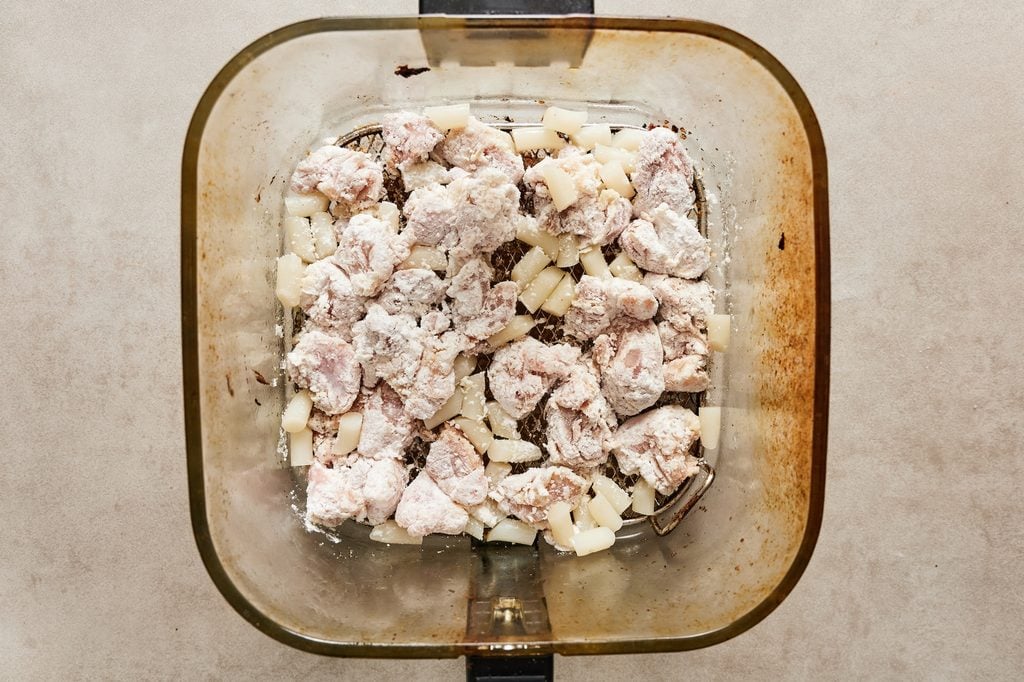 An air fryer basket with chicken pieces and rice cakes before cooking.
